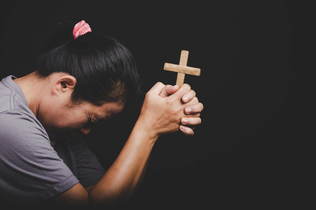 A woman in prayer, holding a crucifix tightly.