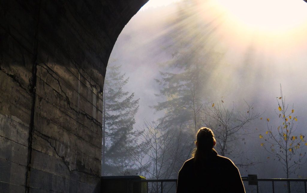 A woman walking out of a tunnel as the sun glares down.