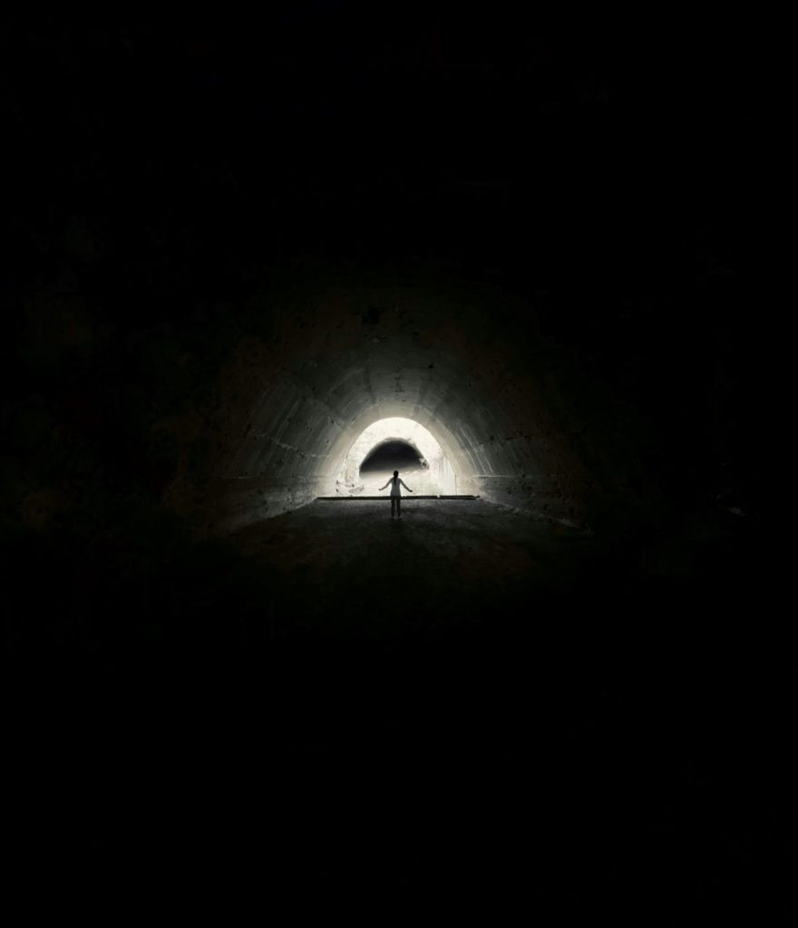 A person inside a dark tunnel with a ray of light at the end.