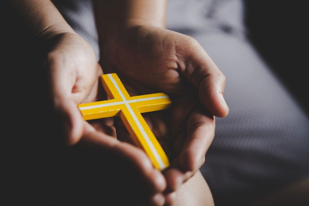 Hands cupped holding a yellow wooden cross.