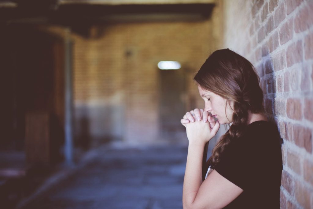 A woman leaning against a wall in prayer.