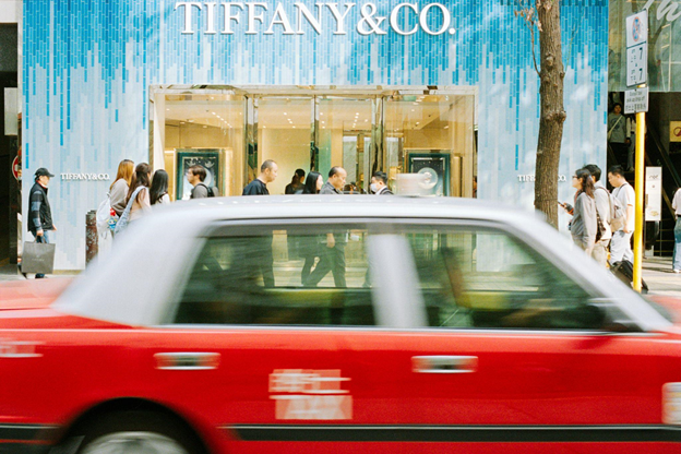 Red taxi blurs past pedestrians in front of a store.