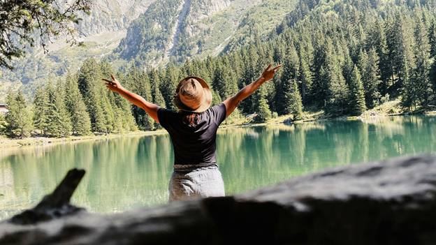 A person stands with arms raised by a serene mountain lake, evoking a sense of freedom and hope.