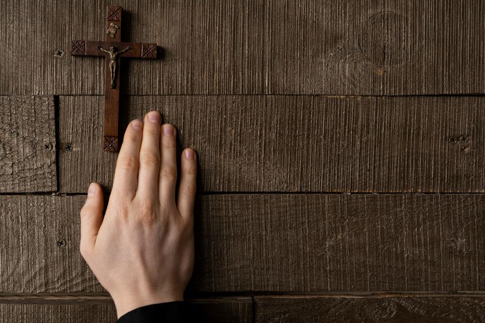 A hand touching the base of a wooden cross.