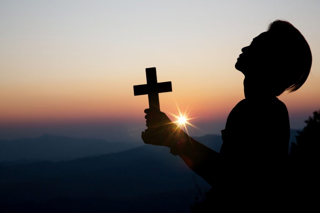 Silhouette of a man holding up a cross as the sun rises.