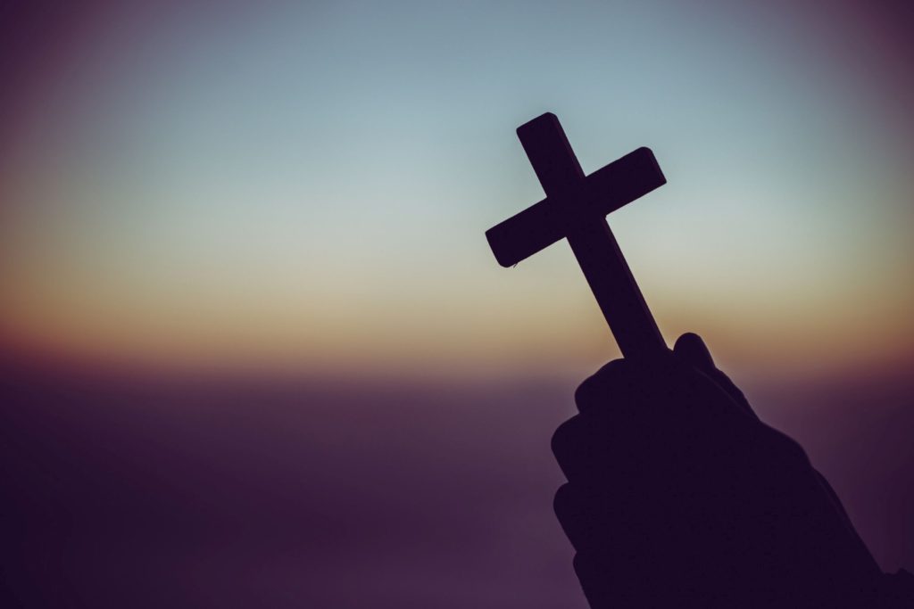 A pair of hands holding a cross at dawn.